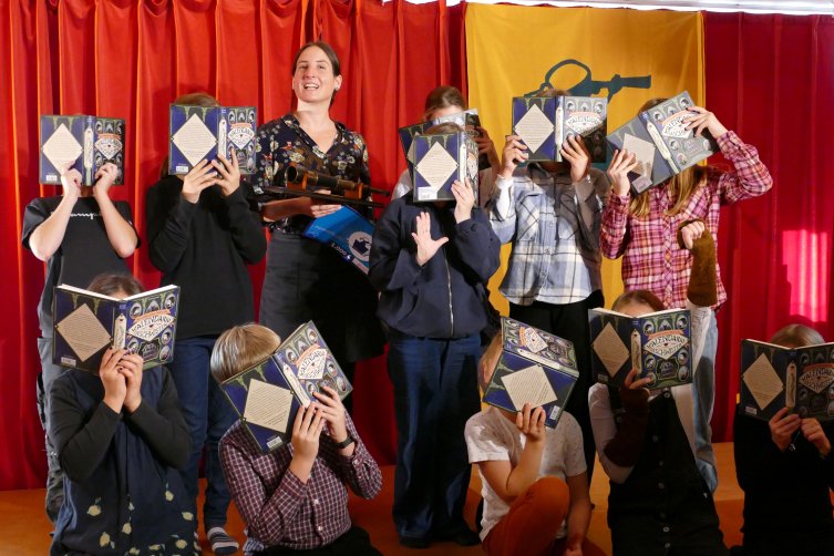 Gruppenfoto der Kinderjury mit Louisa Söllner. Die Kinder halten sich Söllners Buch vors Gesicht