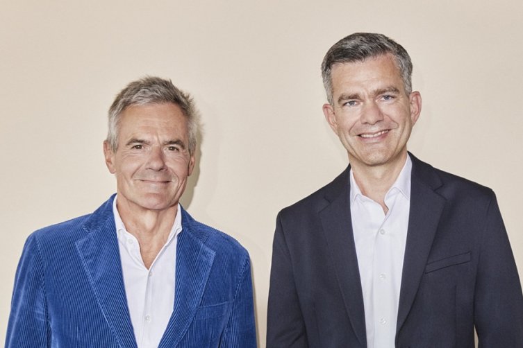 Rainer Esser und Nils von der Kall im Anzug vor einer Wand